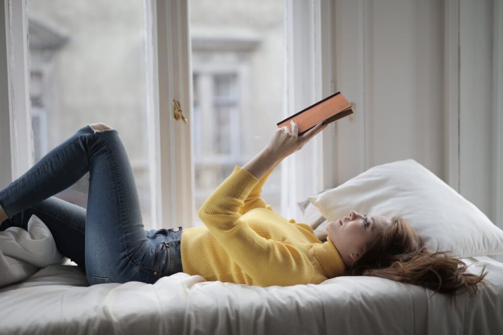 a lady is reading while lying down flat on bed